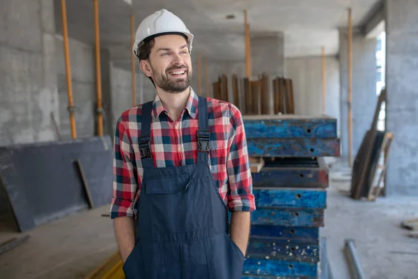 Stavební dělník v helmě a kostkované košili, ruce v kapsách — Stock fotografie