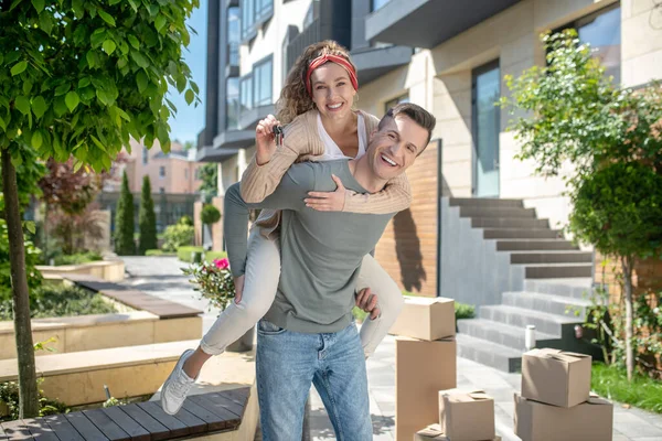 Mujer sonriente sentada sobre sus maridos y mostrando las llaves — Foto de Stock