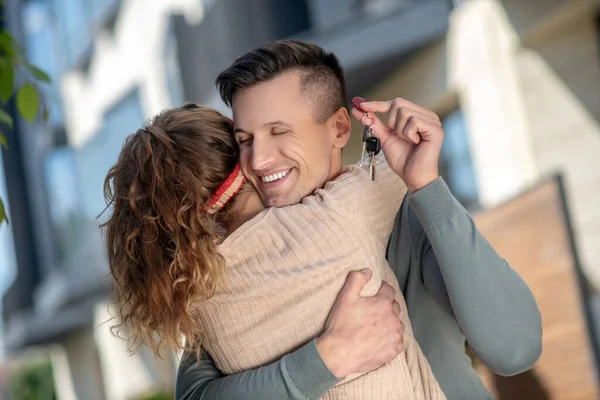 Jovem casal segurando a chave da nova casa e abraçando — Fotografia de Stock