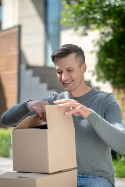 Sonriente hombre guapo de pelo oscuro abriendo un cartón — Foto de Stock