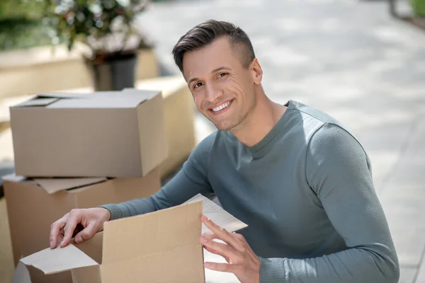 Sonriente hombre guapo sentado junto a las cartulinas — Foto de Stock