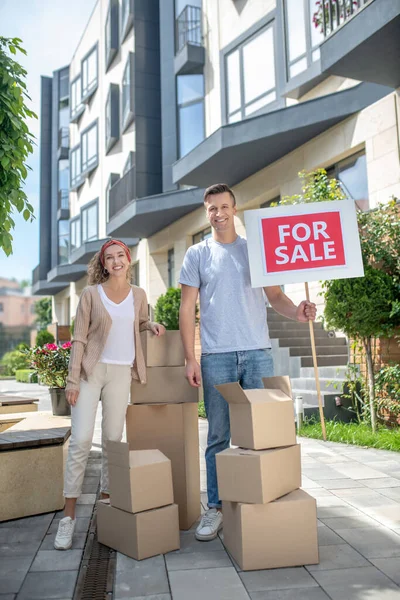 Sonriendo feliz pareja de pie cerca de cartulinas sintiéndose listo para mudarse a un nuevo apartamento — Foto de Stock