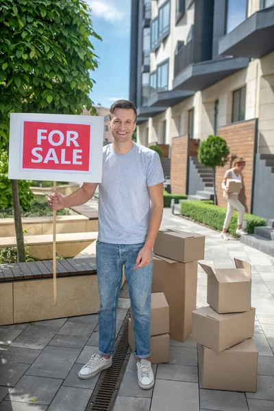 Joven sonriente de pie con una mesa en venta — Foto de Stock