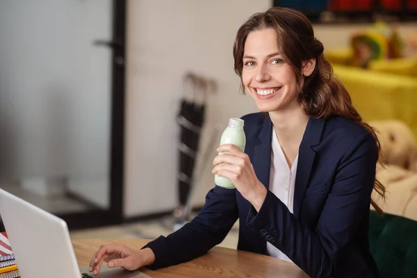 Souriante fille avec bouteille de yaourt dans le bureau à l'ordinateur portable — Photo