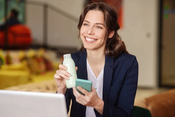 Joyeuse fille avec une petite bouteille blanche et un smartphone — Photo