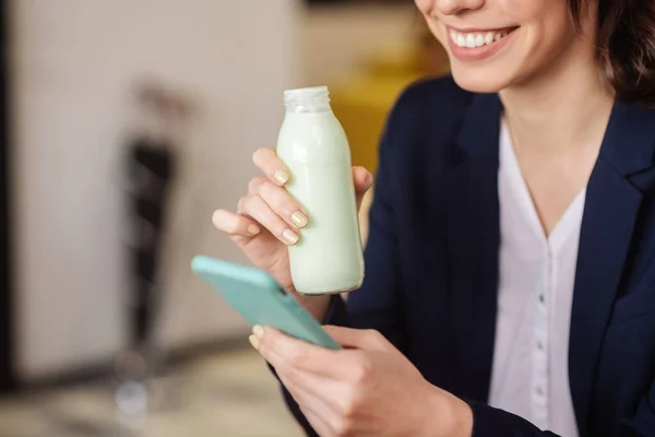 Manos femeninas sosteniendo una botella pequeña y un teléfono inteligente — Foto de Stock