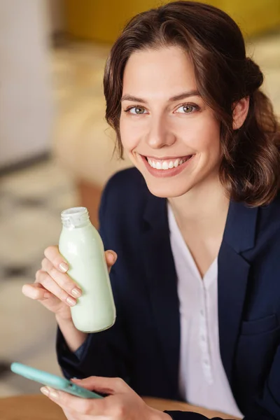 Hermosa chica con ojos marrones sosteniendo yogur y teléfono inteligente — Foto de Stock