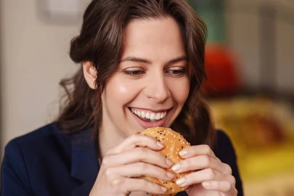 Spokojená žena jí hamburger v kanceláři. — Stock fotografie