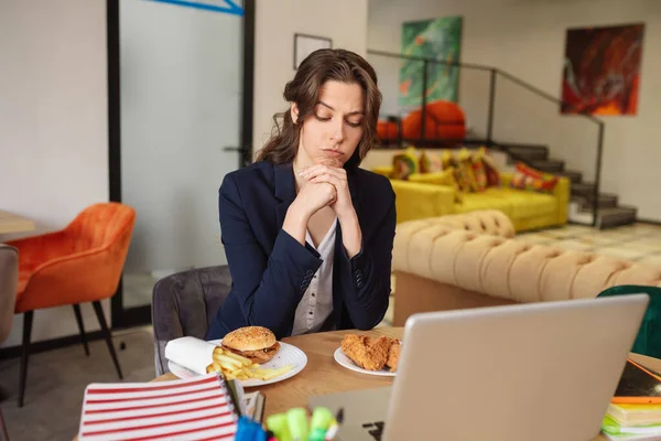 Pensando jovem mulher sentada e olhando para a comida em pratos — Fotografia de Stock