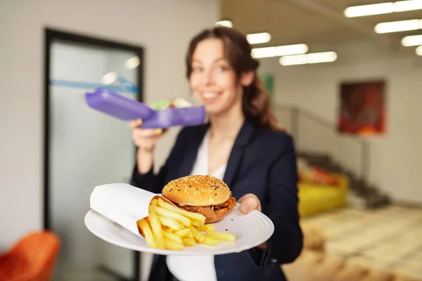 Chica feliz sosteniendo un plato con hamburguesa y papas fritas — Foto de Stock