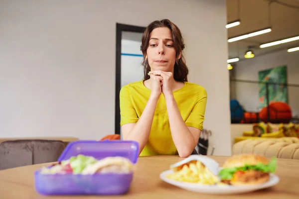 Молодая нерешительная женщина смотрит на еду за столом — стоковое фото