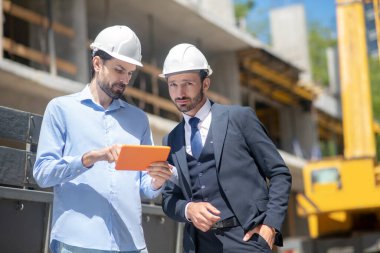 Foreman, tabletinde bina yöneticisine bir şey gösteriyor.