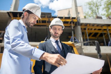 Bina yöneticisi ve ustabaşı binanın önünde duruyor, planı tartışıyorlar.