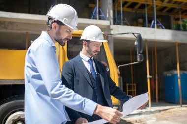 Binanın önünde duran bina yöneticisi ve ustabaşı dikkatle plan üzerinde çalışıyor.