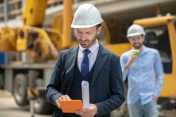 Supervisor de construção verificando algo no tablet, capataz de pé atrás dele com xícara de café — Fotografia de Stock