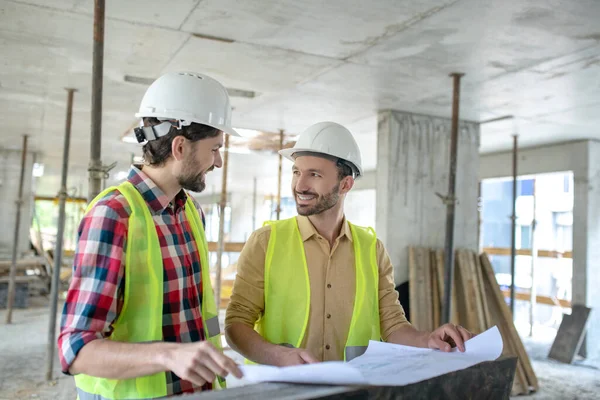 Trabalhadores da construção em coletes amarelos brainstorming sobre o modelo, discutindo-o — Fotografia de Stock