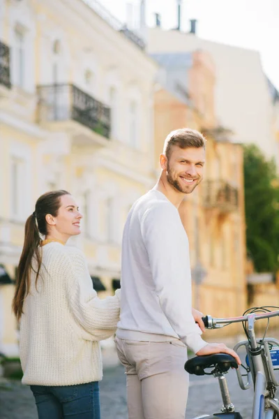Улыбающийся мужчина с велосипедом и женщина смотрит на него — стоковое фото