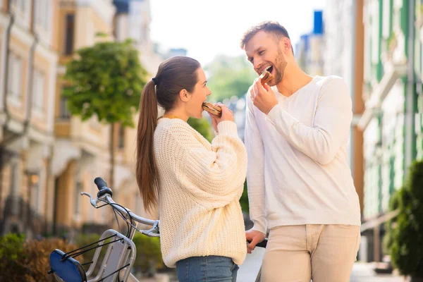 Alegre hombre y mujer mordiendo bocadillos en la calle —  Fotos de Stock