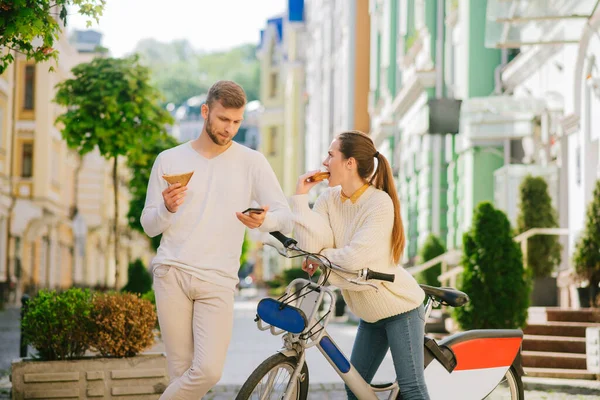 Hombre mirando el teléfono inteligente, mujer con bicicleta comer sándwich — Foto de Stock