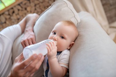 Babasının elleri küçük oğlu için sütle şişeyi tutuyor.
