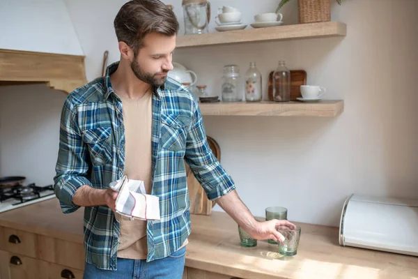 Jongeman in een geruit shirt zet het schone glas op tafel — Stockfoto