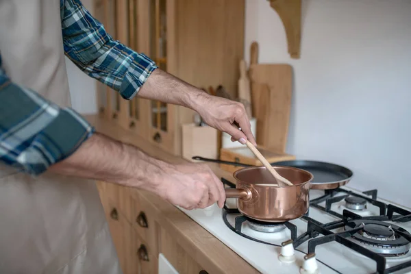 Mann in kariertem Hemd und Schürze stellt Pfanne auf den Ofen — Stockfoto