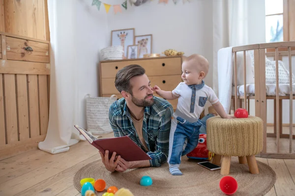 Father in a checkered shirt holding a book looking at his son standing next to him