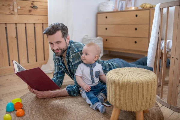 Vater im karierten Hemd liest seinem niedlichen kleinen Jungen ein Buch vor — Stockfoto