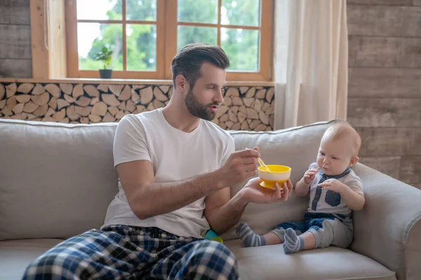 Junger Vater hält den Teller und füttert das Baby — Stockfoto