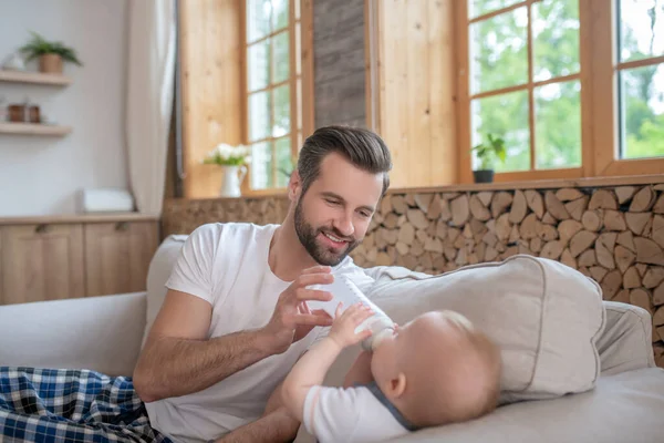 Schöner Vater füttert das Baby aus der Flasche und lächelt — Stockfoto