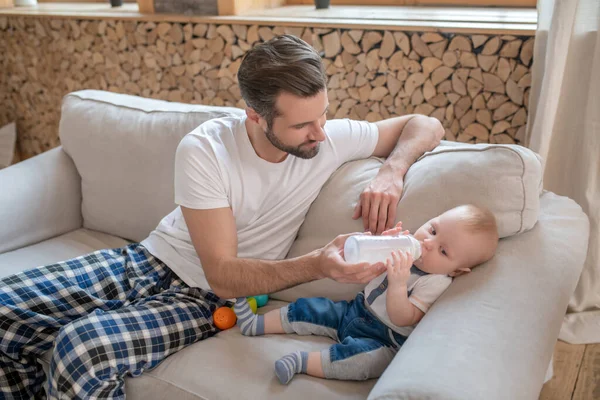 Padre alimentando al bebé desde el biberón y sintiéndose feliz — Foto de Stock