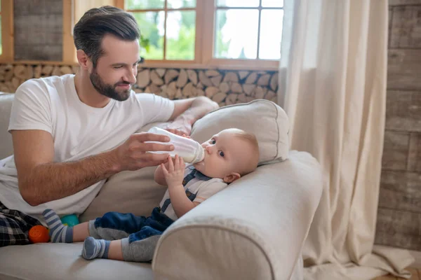 Vater füttert das Baby aus der Flasche und lächelt — Stockfoto