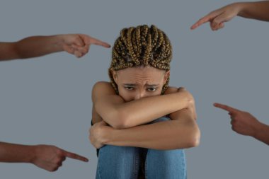 Üzgün genç Afrikalı Amerikalı dizlerini tutuyor, dört el onu işaret ediyor.