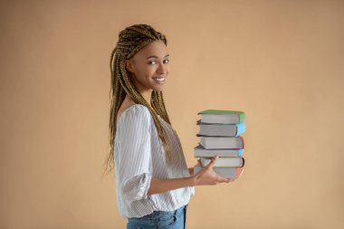 Genç, mutlu, Afro-Amerikan kadın önünde bir yığın kitap taşıyor.
