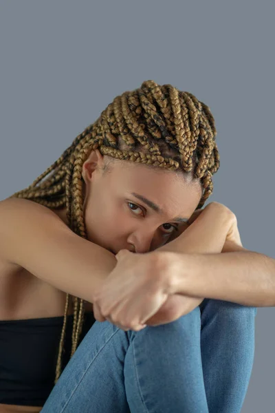 Traurige junge Afroamerikanerin hält ihre Knie und stützt ihren Kopf auf ihre Arme — Stockfoto