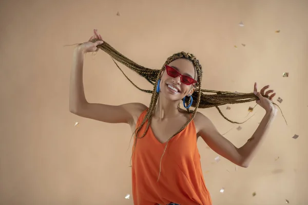 Улыбающаяся юная афроамериканка танцует, играя со своими дредами под блестками — стоковое фото