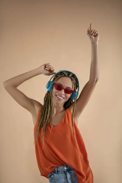 Улыбающаяся молодая афроамериканка в наушниках, поднимающая руки, танцующая — стоковое фото