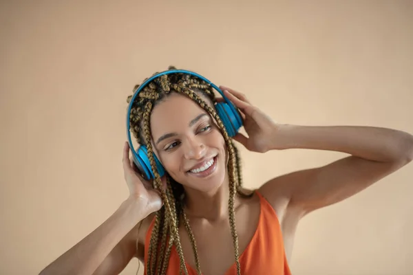 Glimlachende jonge Afro-Amerikaanse vrouw, aanraken van blauwe koptelefoon en luisteren naar muziek — Stockfoto