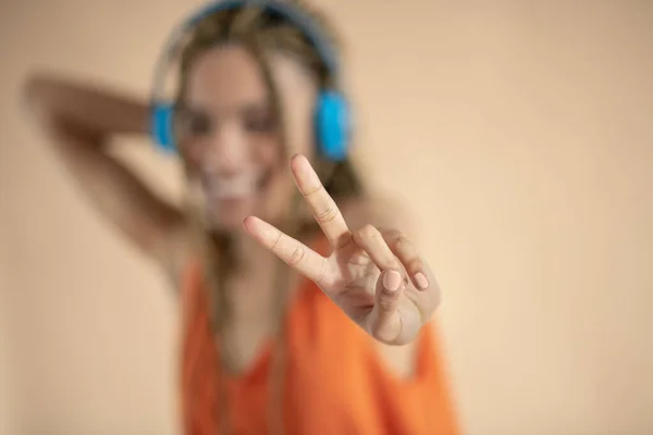 Glimlachende jonge Afro-Amerikaanse vrouw in blauwe koptelefoon, luisteren naar muziek, vredesbord tonen — Stockfoto