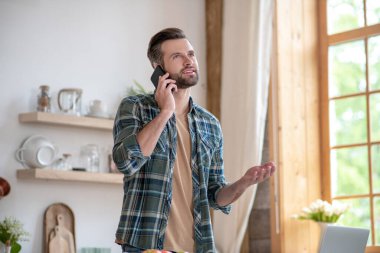 Kareli gömlekli bir adam telefonda konuşuyor ve heyecanlı görünüyor.