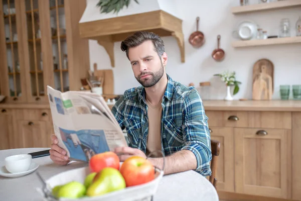 Чоловік у картатій сорочці, сидячи за столом, читаючи газету і дивлячись залучені — стокове фото