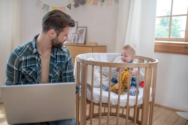Donkerharige vader werkt op een laptop terwijl zijn zoontje speelt — Stockfoto