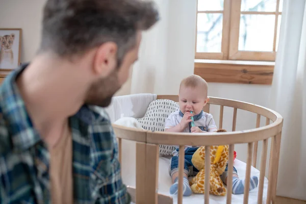 Dunkelhaariger Vater beobachtet seinen kleinen Sohn beim Spielen im Laufstall — Stockfoto