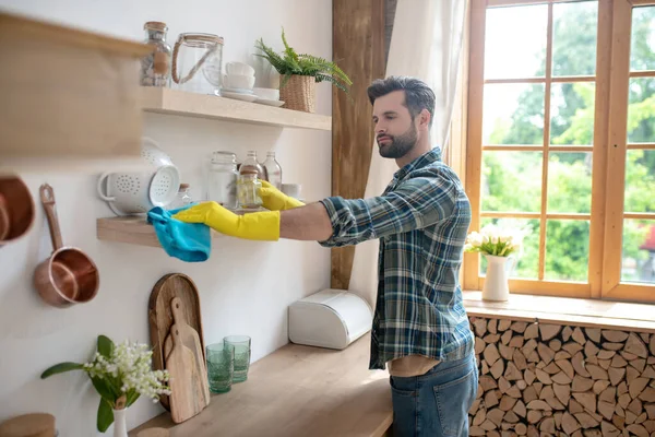 Donkerharige man in gele handschoenen maakt de keuken schoon en ziet er betrokken uit — Stockfoto