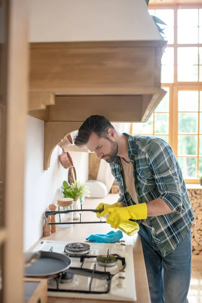 Чоловік в жовтих рукавичках стоїть і прибирає піч на кухні — стокове фото