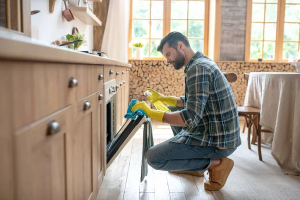 Man in yellow gloves sitting and cleaning the surface in the kitchen — Stock Photo, Image