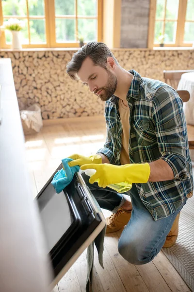 Hombre con guantes amarillos limpiando la superficie en la cocina y buscando ocupado — Foto de Stock