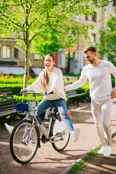 Mujer alegre en bicicleta y hombre atento corriendo cerca — Foto de Stock