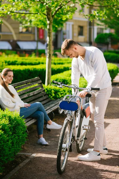Hombre atento inspeccionando bicicleta hombre y mujer en un banco — Foto de Stock