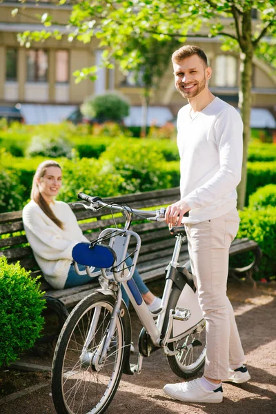 Kvinna på bänk och man stående med cykel — Stockfoto